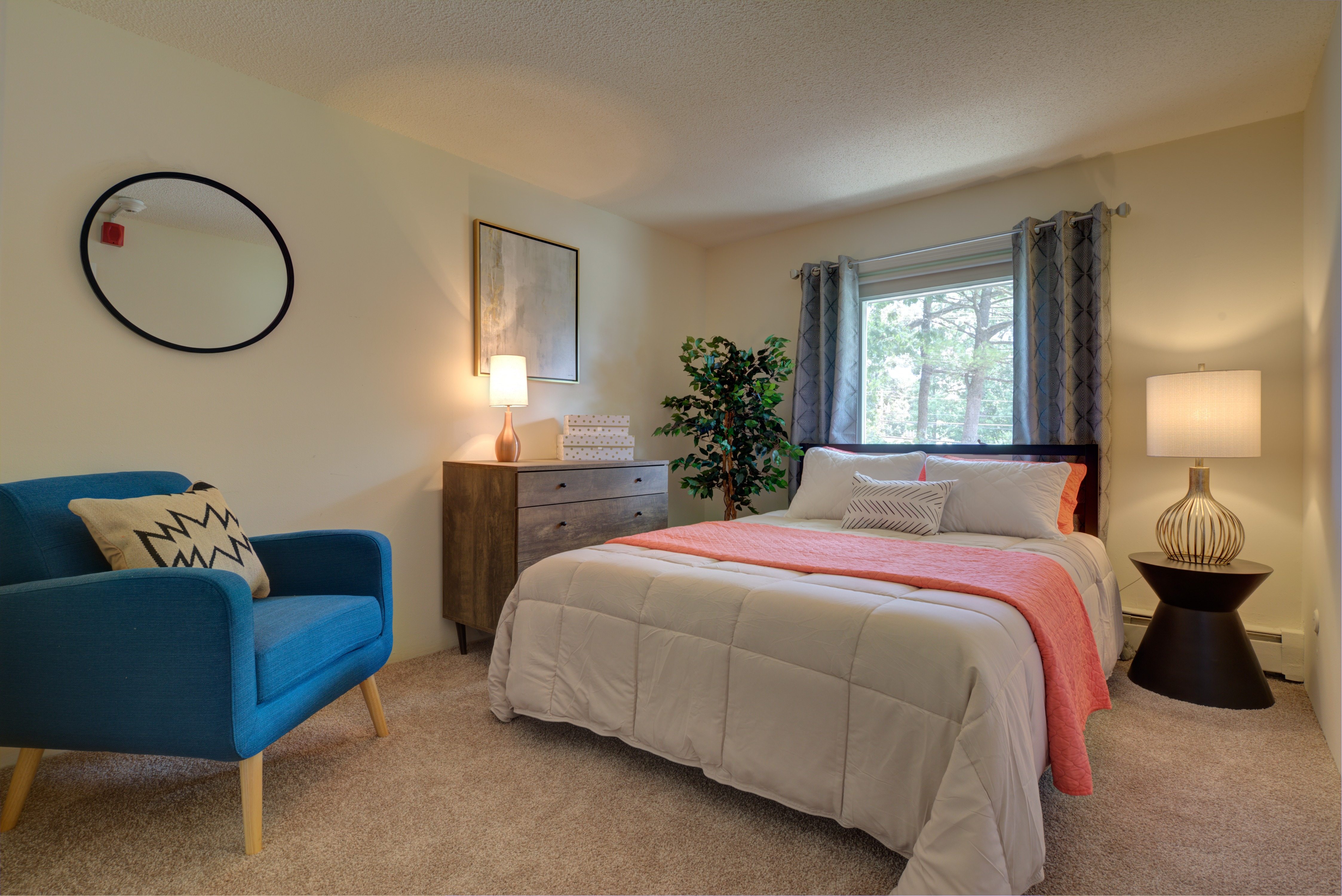 A bedroom with a bed, a blue chair, and a plant.